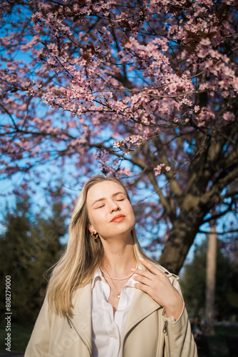 Fashion outdoor photo of beautiful woman with blond hair in elegant suit posing in spring flowering park with blooming cherry tree. Copy space and empty place for advertising text © satura_