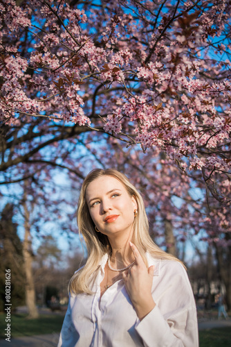 Woman with cherry flowers surrounded by blossoming trees copy space. Beauty and seasonal change and spring bloom season concept. © satura_