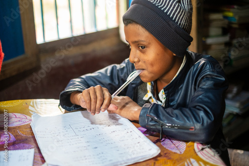 South asian school going boy solving mathematics homework , indoor image of a student writing in a notebook 