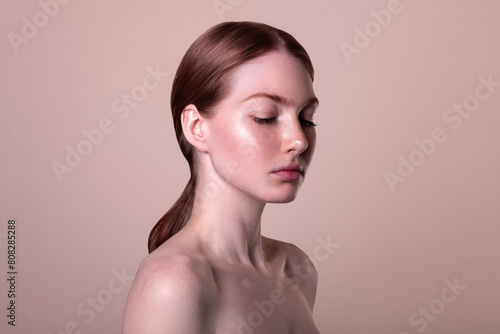 Skin care, natural beauty, clear glow skin no makeup, portrait of a beautiful young red-haired woman with freckles isolated on beige background