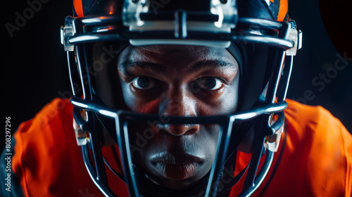 Close-up of a focused american football player wearing a helmet and game attire, showcasing determination and passion against a dark background. Ideal for sports themes and athletic determination photo