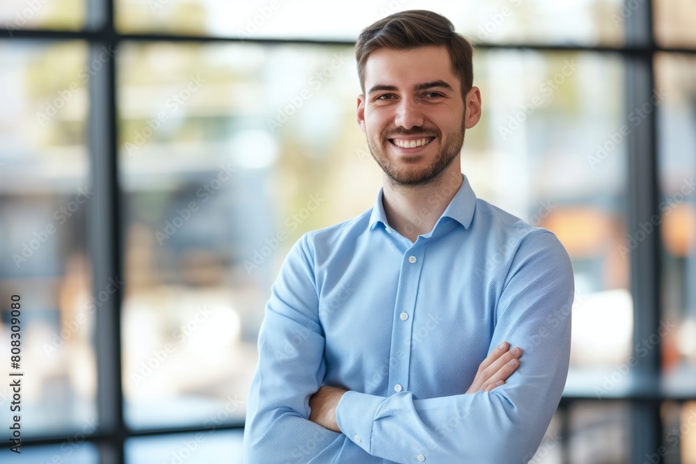 Professional young man smiles warmly, standing with crossed arms in a modern office environment, exuding confidence and approachability with natural daylight enhancing the friendly atmosphere Professional young man smiles warmly, standing with crossed arms in a modern office environment, exuding confidence and approachability with natural daylight enhancing the friendly atmosphere