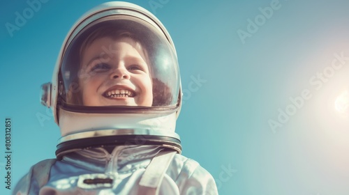 Cheerful child in an astronaut helmet beams with joy against a clear blue sky, embodying dreams of space exploration and the innocence of youthful ambition