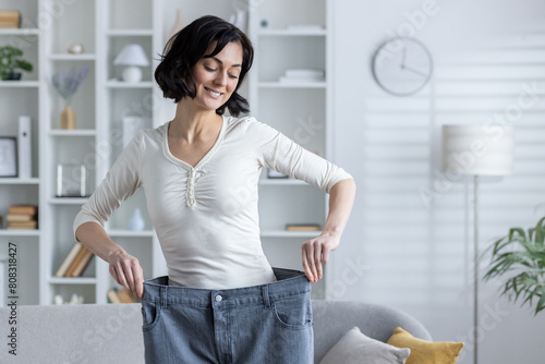 Cuadro en lienzo Slim and beautiful young woman standing at home near sofa wearing baggy pants, h