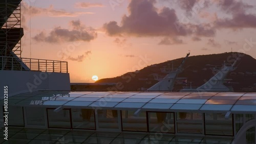 Sun rises over hill of Sint Maarten, illuminating structural details of upper deck at cruise ship photo
