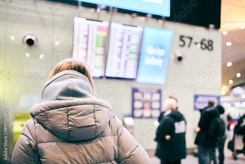 An unrecognizable woman in casual clothes stands with her back to the camera looking at the departure board. People are standing near the screen and checking the departure time. High quality photo photo