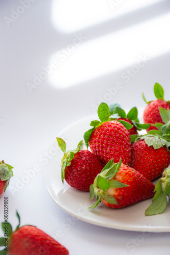 Several fresh red strawberries on a plate on a white background
