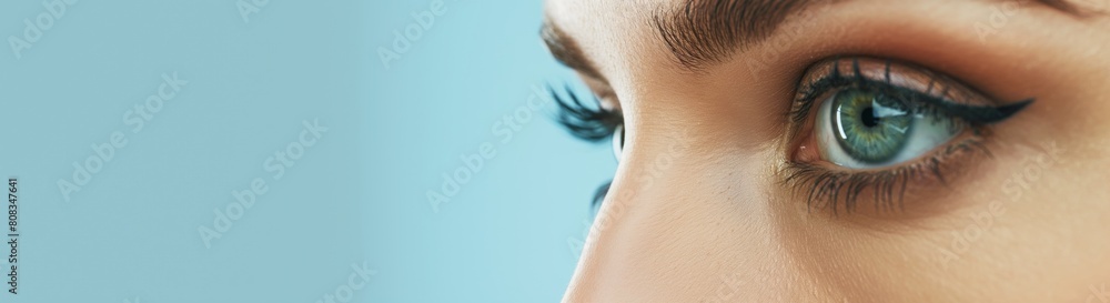 Naklejka premium Detailed close-up image capturing the beautiful eyes of a woman with perfectly applied mascara, set against a soft blue background highlighting her gaze and eyelashes