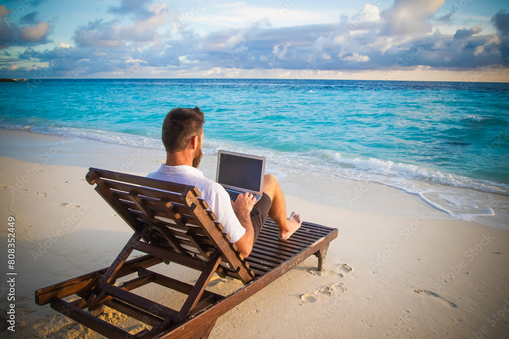 man working on laptop on tropical beach