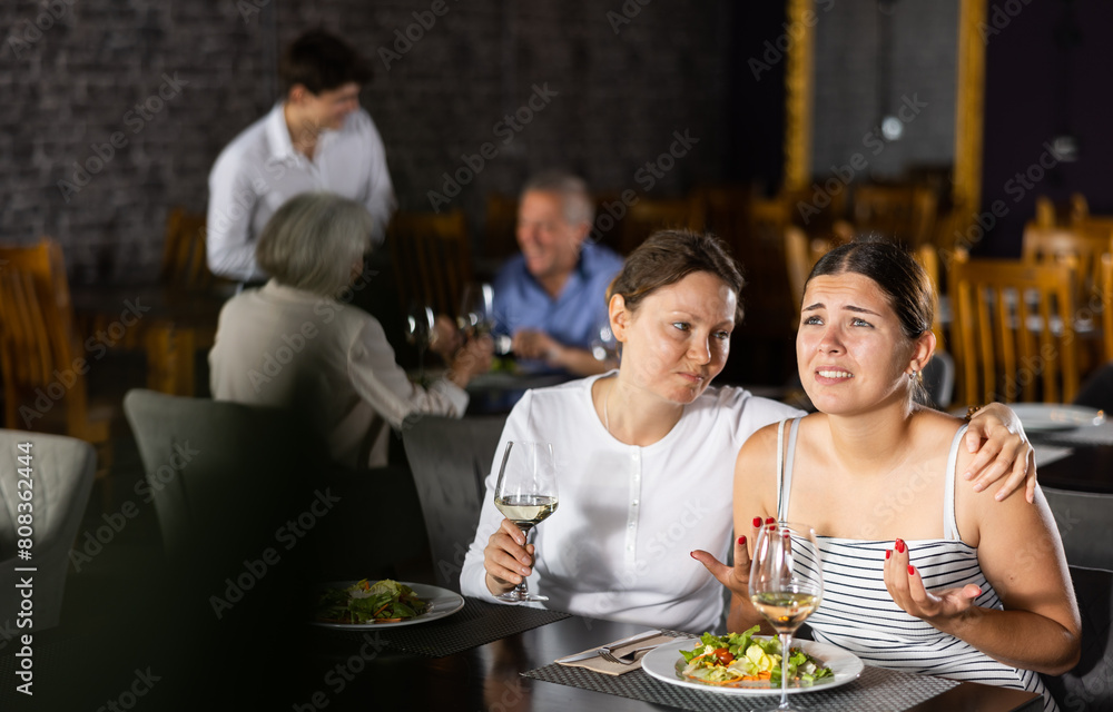 Young woman and adult woman have dinner and drink wine together in restaurant
