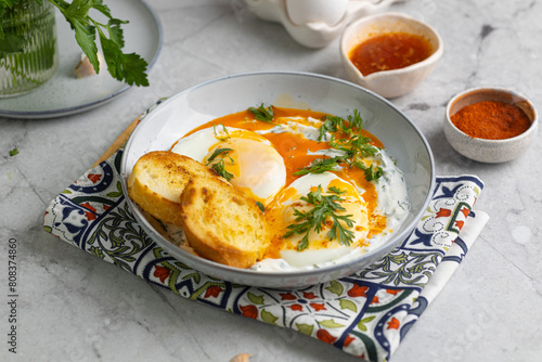 Cilbir or Turkish Eggs. poached eggs topped over herbed greek yogurt, drizzled with hot spiced paprika olive oil. Turkish breakfast in a grey bowl on marble background. shakshuka with pepper photo