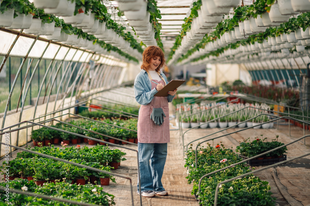 Φωτογραφία Ginger botanist writing down in clipboard at greenhouse.