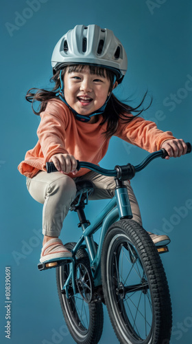 happy asian child riding bicycle and smiling at camera isolated on blue