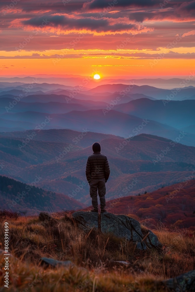 Solitary figure admires autumn sunrise over mountain 
