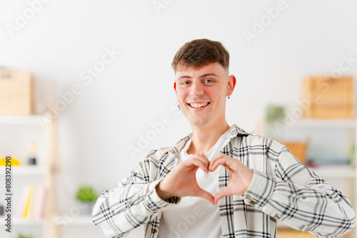 Smiling cute young man join hands forming heart shape standing at home
