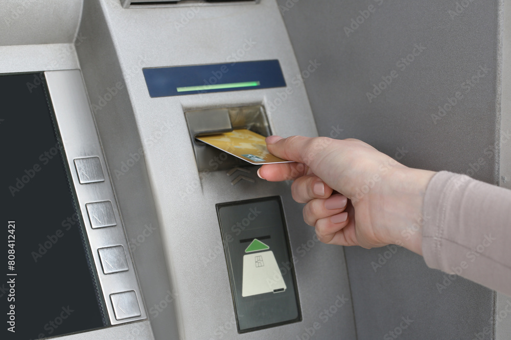 Woman inserting credit card into grey cash machine, closeup Woman inserting credit card into grey cash machine, closeup