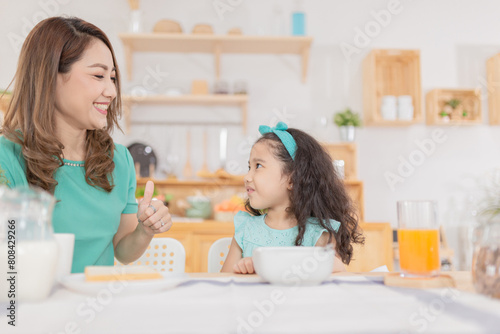 Asian children and her mom have a breakfast in the morning, asian mother feeling glad and show thumbs up sign with her hand, child nutrition and development, they feeling happy in family time