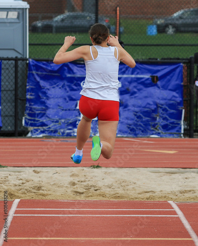 Girl in the air while jumping into the sand pit during a track meet