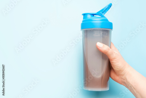 Hand holds a shaker with a protein shake on blue background.