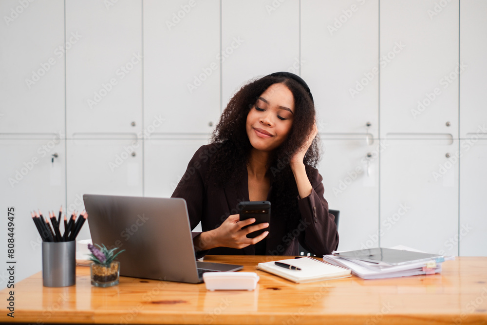 Relaxed and content young professional using her smartphone with a gentle smile at her office desk. Relaxed and content young professional using her smartphone with a gentle smile at her office desk.