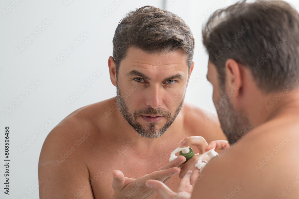 Fototapeta premium Beauty man applying face cream. Skincare cream, skin anti-aging wrinkle effect. Man applying moisturizer cream on skin. Skin care, cosmetic cream treatment for male face. Male skin care beauty.