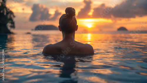 Silhouette einer Frau mit hochgesteckten Haaren in einem Infinity Pool genießt entspannt den Ausblick auf einen Sonnenuntergang, Sommer Urlaub Entspannung Konzept