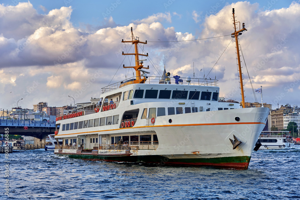 Istanbul, Turkey - September 6, 2022: Ferry boat sailing in Bosphorus Strait, with Istanbul skyline in the background, overlooking Galata Bridge.