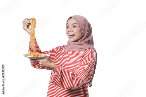 A portrait of a happy Asian woman hijab wearing a red white shirt, eating noodles. Isolated against a white background.