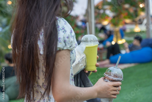 A young woman holds a disposable cup of smoothie outside in the park