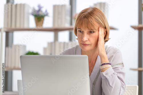Worried caucasian woman using laptop to check their bills at home