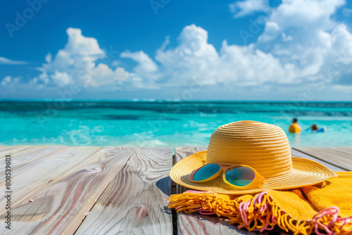 A straw hat and sunglasses are on the beach. The scene is bright and sunny, with the sun shining down on the sand