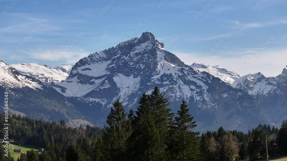 High snowy alpine mountains. Coniferous forests in the valley with the mountain village of Amden. Switzerland from the perspective of a drone High snowy alpine mountains. Coniferous forests in the valley with the mountain village of Amden. Switzerland from the perspective of a drone