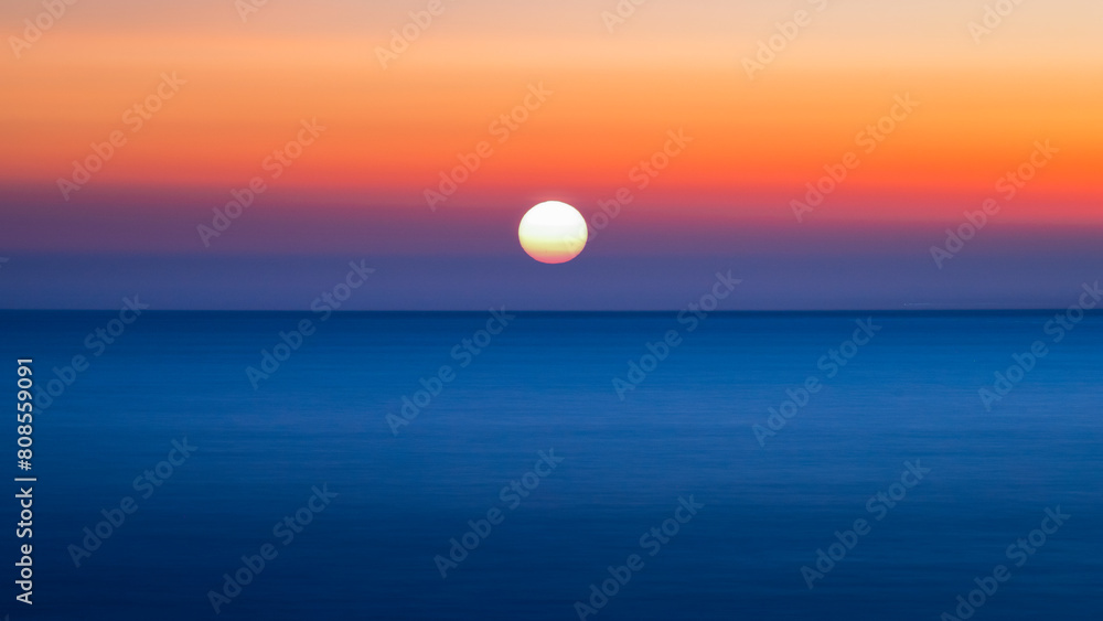 The orange spherical sun was about to set behind the horizon on the surface of the sea. The sky is colorful and beautiful.