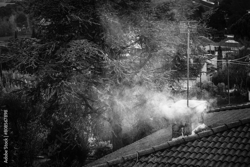 Roof of a house with a chimney releasing smoke into the atmosphere.