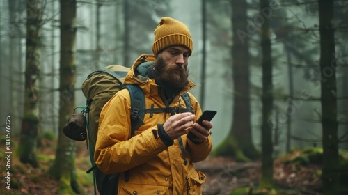 Bearded hiker with backpack walks through forest, holding smartphone