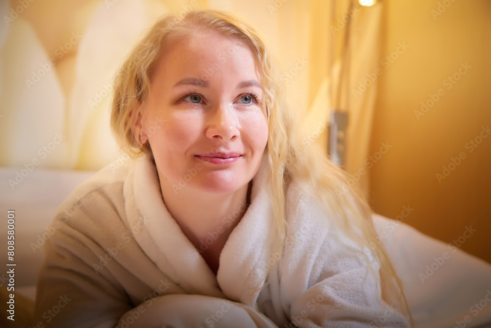 A blonde girl in a white terry bathrobe in a hotel room after spa treatments on a trip or travel. Weekend and vacation body care A blonde girl in a white terry bathrobe in a hotel room after spa treatments on a trip or travel. Weekend and vacation body care