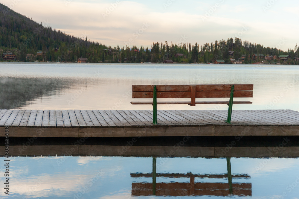 Naklejka premium Empty bench on a misty lakeside dock at dawn