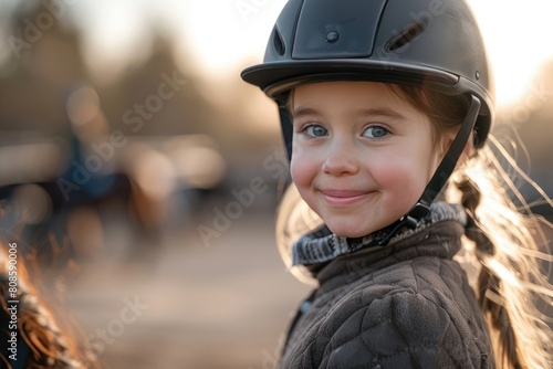 Happy girl kid at equitation lesson looking at camera while riding a horse, wearing horse-riding helmet