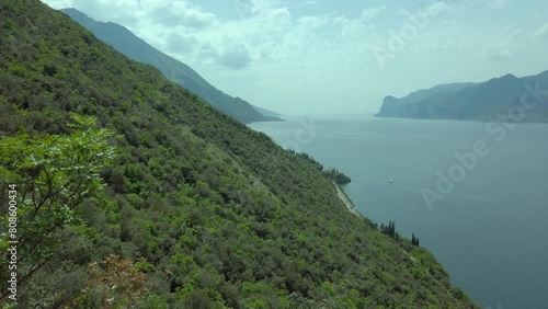 Panoramic view of Lake Garda from the trekking path on the Busatte mountain in Torbole, amidst a backdrop of clear skies, clouds, and lush vegetation, showcasing the natural beauty photo