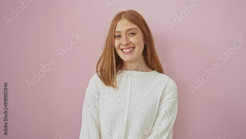Cute redhead woman winking cheekily at the camera, happy and cheerful face aglow. dressed casually in sweater, her flirtatism shines against isolated pink wall background. photo