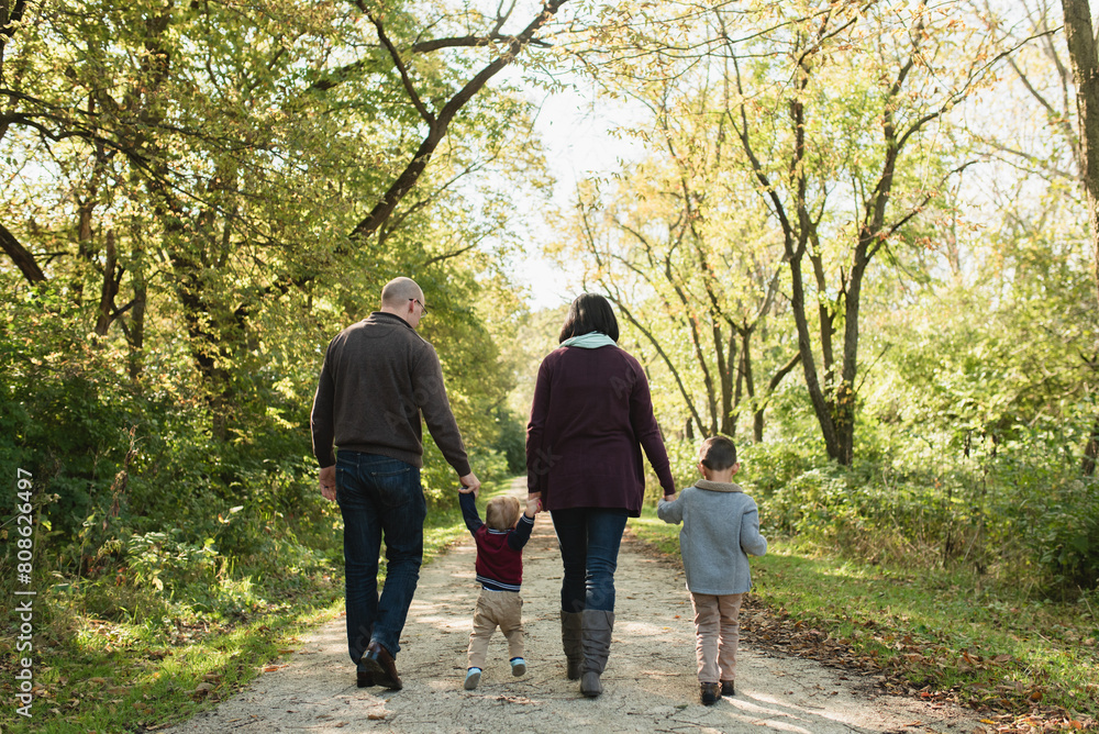 Back view of young family holding hands and walking away in forest Back view of young family holding hands and walking away in forest