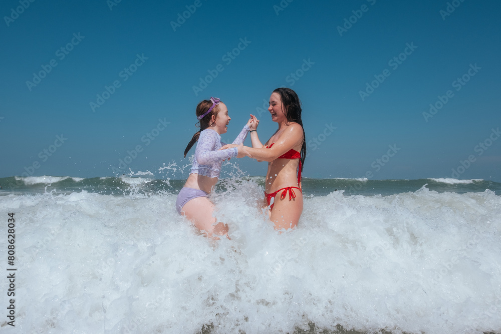 Happy sisters laughing while waves hit them in ocean Happy sisters laughing while waves hit them in ocean