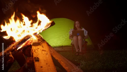 digital nomad working remotely from remote destination in front of bonfire while camping outdoor  photo