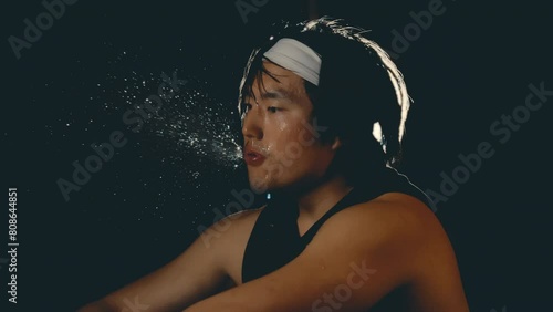 Asian male athlete spitting water in slow motion after hard workout in dark gym, backlit close up 4k 800fps photo