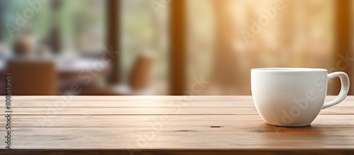A porcelain coffee cup utensil sits on a wooden table top with a blurred background featuring the interior of a living room This is a copy space image
