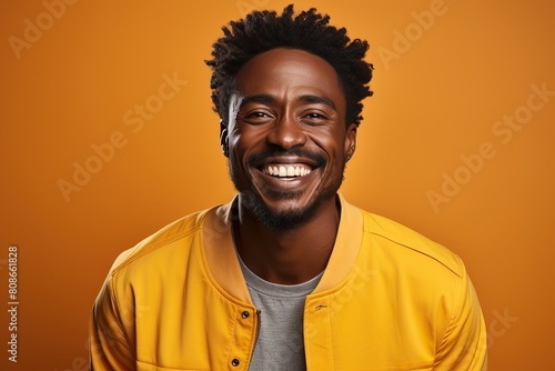 Smiling black man in a yellow jacket on a yellow background. © Niko_Dali