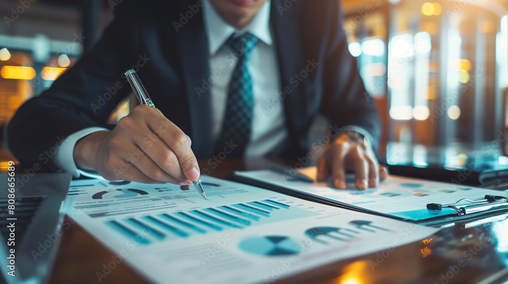Business professional analyzing financial statistics on documents with a pen and laptop on desk. Business professional analyzing financial statistics on documents with a pen and laptop on desk.
