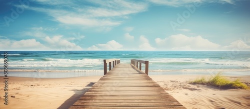 A sandy beach with a wooden path leading to the ocean creating the perfect copy space image