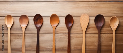 A variety of kitchen utensils including a white wooden spoon a spatula and a clove covered spatula are arranged neatly on a stained light brown wooden board This captivating copy space image is ideal