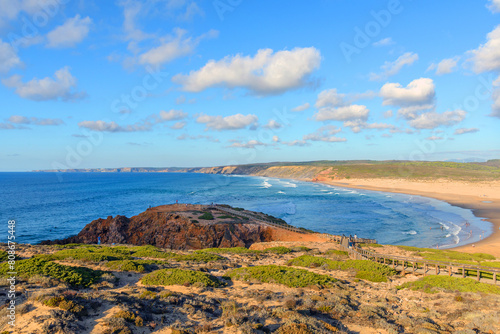 Large beach popular with surfers and tourists against the backdrop of rocky cliffs in Praia da Bordeira, Algarve, Portugal